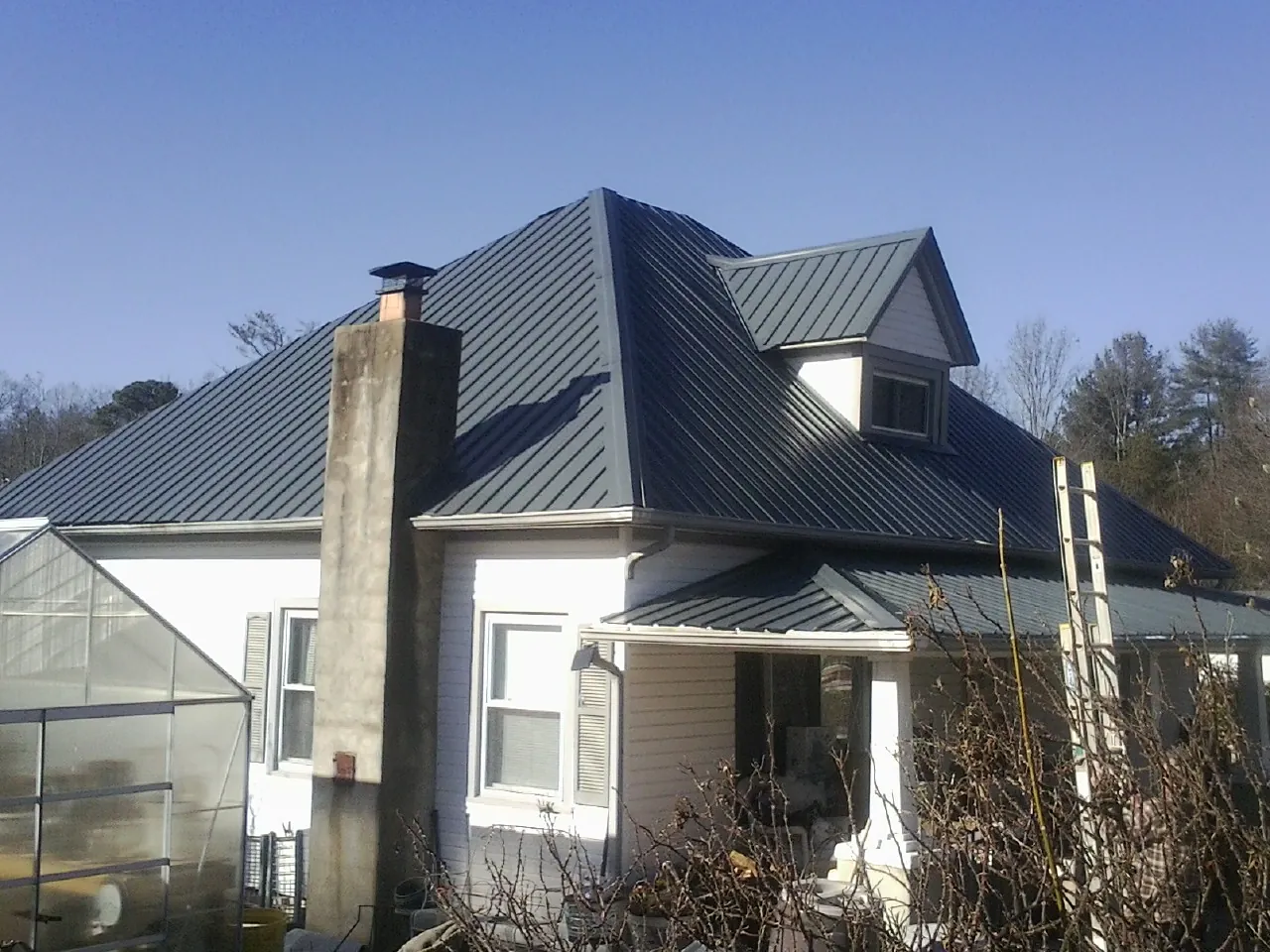 Dark blue standing seam metal roof on a white farmhouse with dormer — Slate & Tile Roof Repair by Roofing Brothers in Hollandale