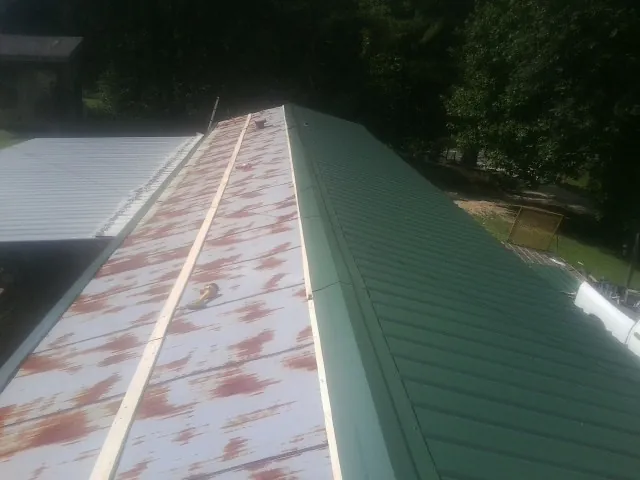 Old rusted panels beside newly installed green metal roofing — Wind Damage Roof Repair by Roofing Brothers in Hollandale