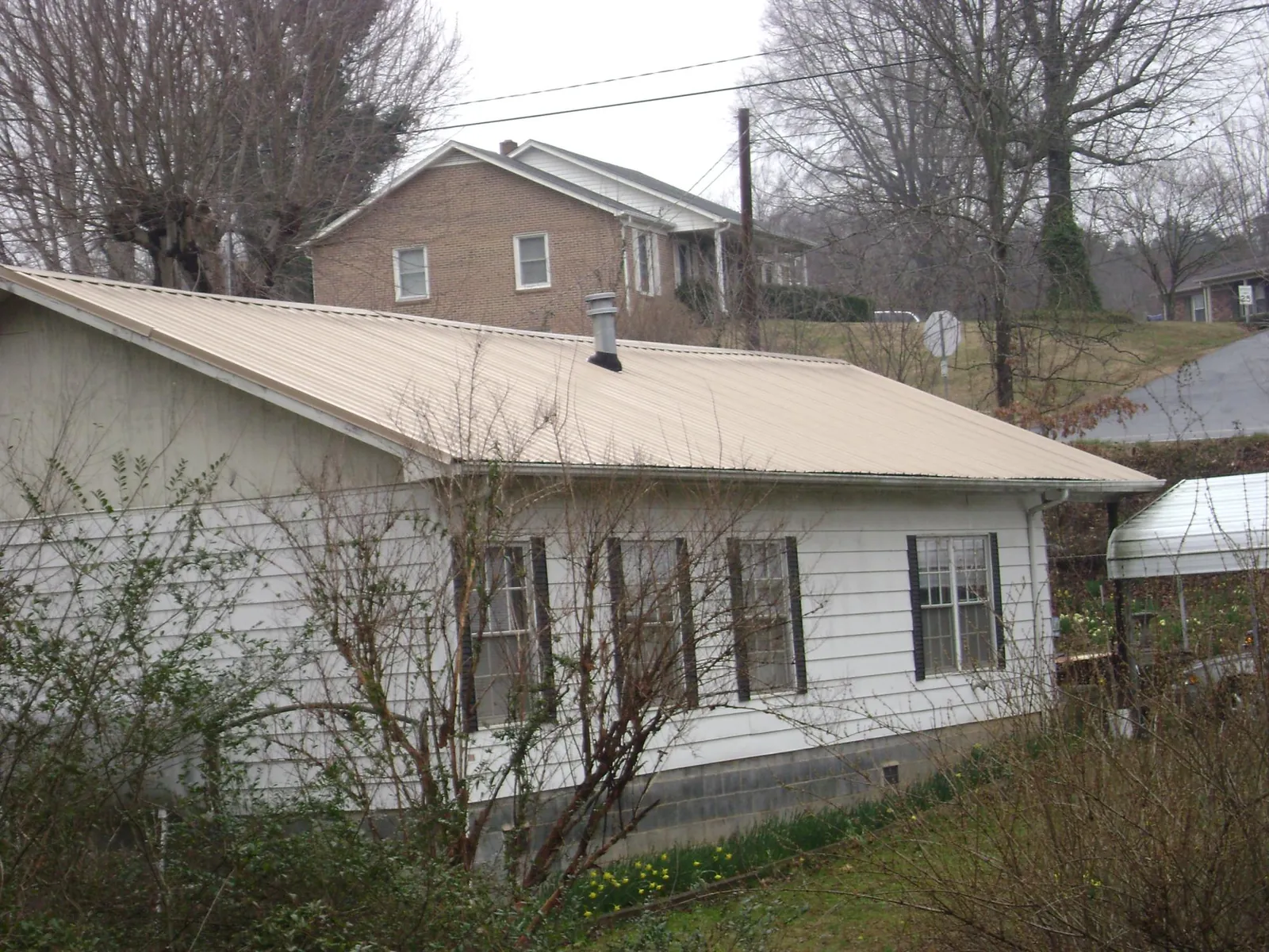 Tan metal roof on a white sided house set into a hillside — Commercial Roofing by Roofing Brothers in Hollandale
